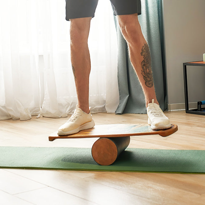 A person stands on a balance board in a bright room, doing an exercise to improve balance and prevent falls.