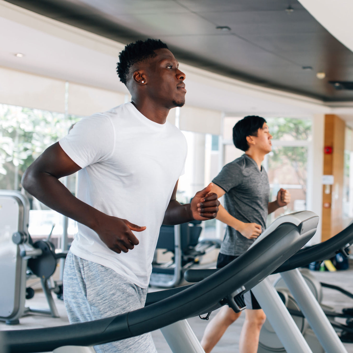 two men run on treadmills at a gym
