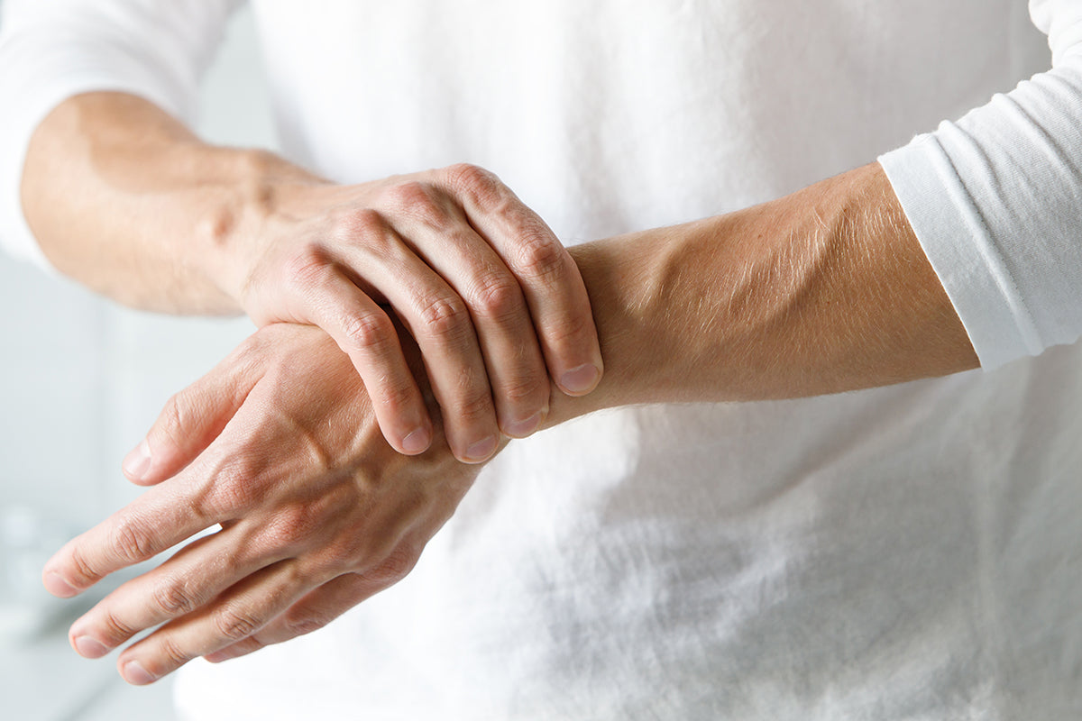 A person wearing a white long sleeve shirt holds their wrist while experiencing painful arthritis symptoms, showing the concept of arthritis pain management strategies.