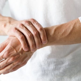 A person wearing a white long sleeve shirt holds their wrist while experiencing painful arthritis symptoms, showing the concept of arthritis pain management strategies.