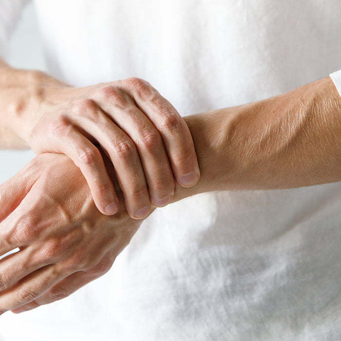 A person wearing a white long sleeve shirt holds their wrist while experiencing painful arthritis symptoms, showing the concept of arthritis pain management strategies.