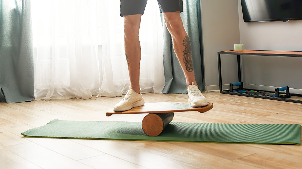 A person stands on a balance board in a bright room, doing an exercise to improve balance and prevent falls.