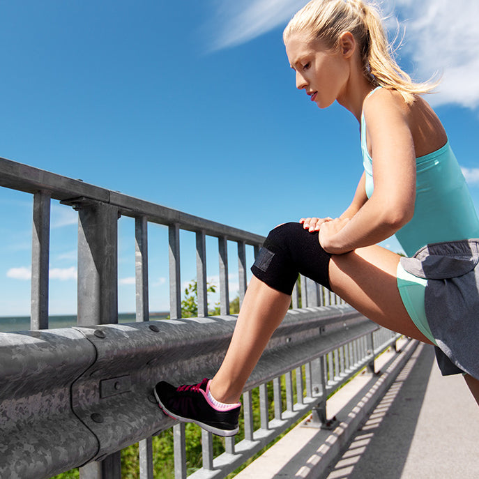 A young, healthy, athletic women in jogging attire stretching her leg and wearing a protective compression knee sleeve while outside on a run