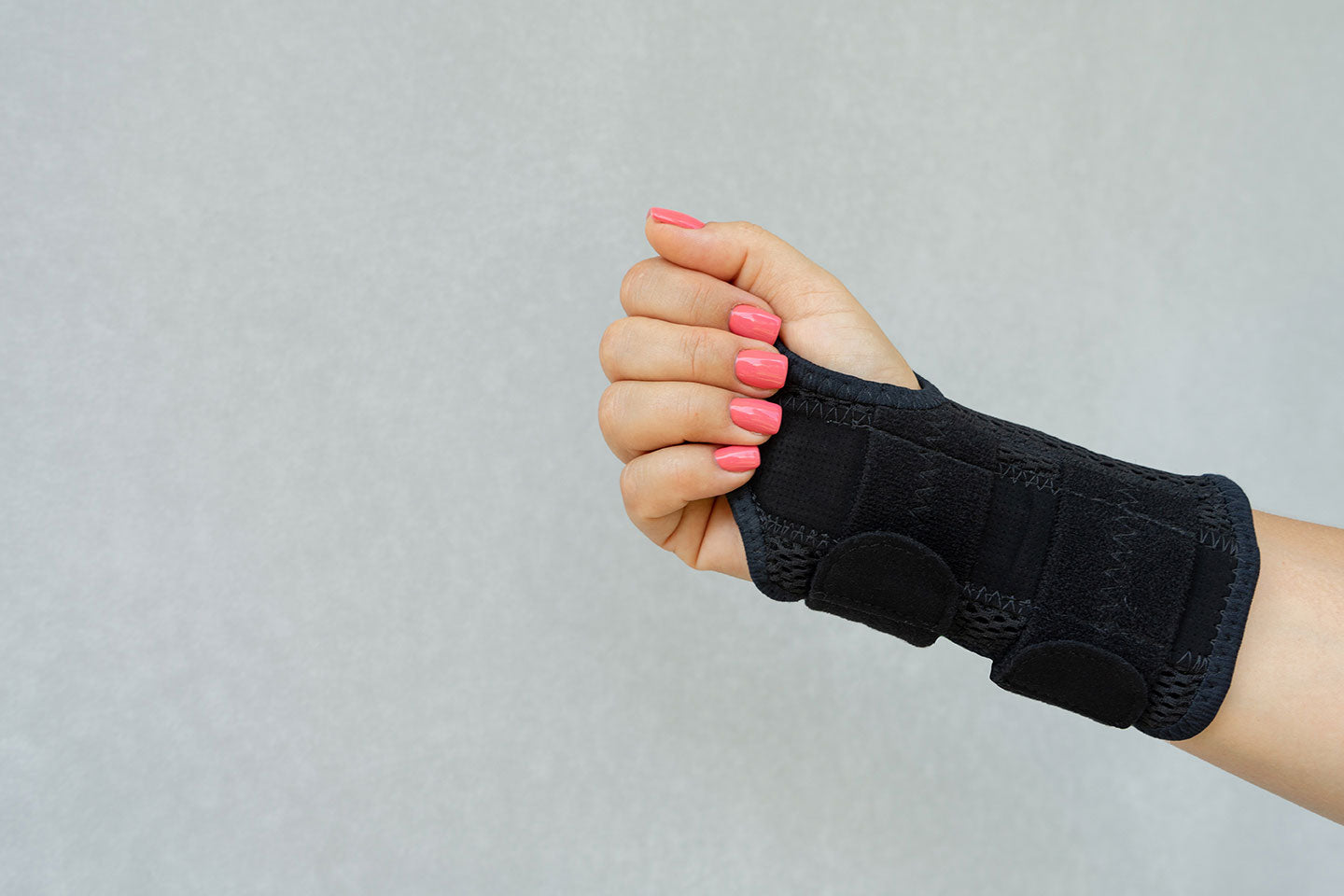 Forearm and hand with pink fingernails in black wrist brace with wrap closure