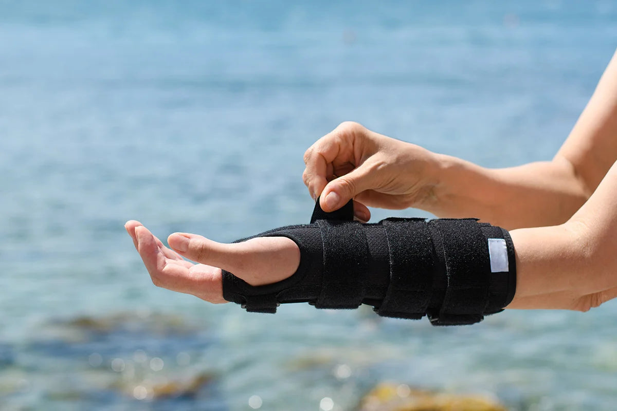 Putting on a wrist brace outdoors, with water in the background