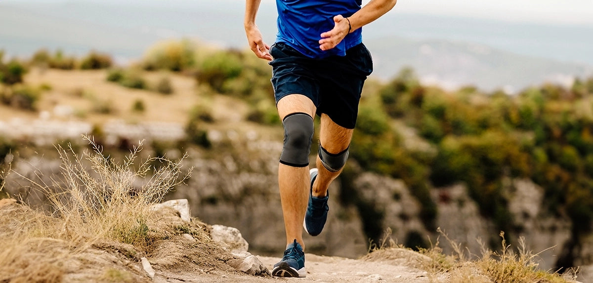 A man running outdoors on a sunny day wearing two lightweight knee compression sleeves