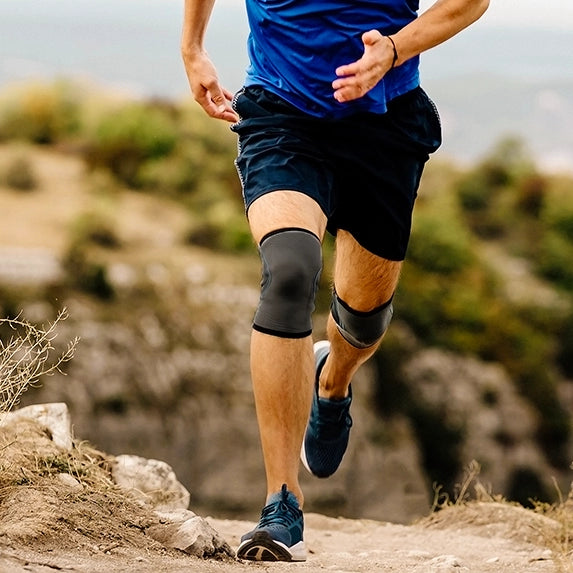 A man running outdoors on a sunny day wearing two lightweight knee compression sleeves