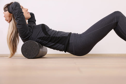 Woman with long blond hair wearing black workout clothes while rolling on a black foam roller