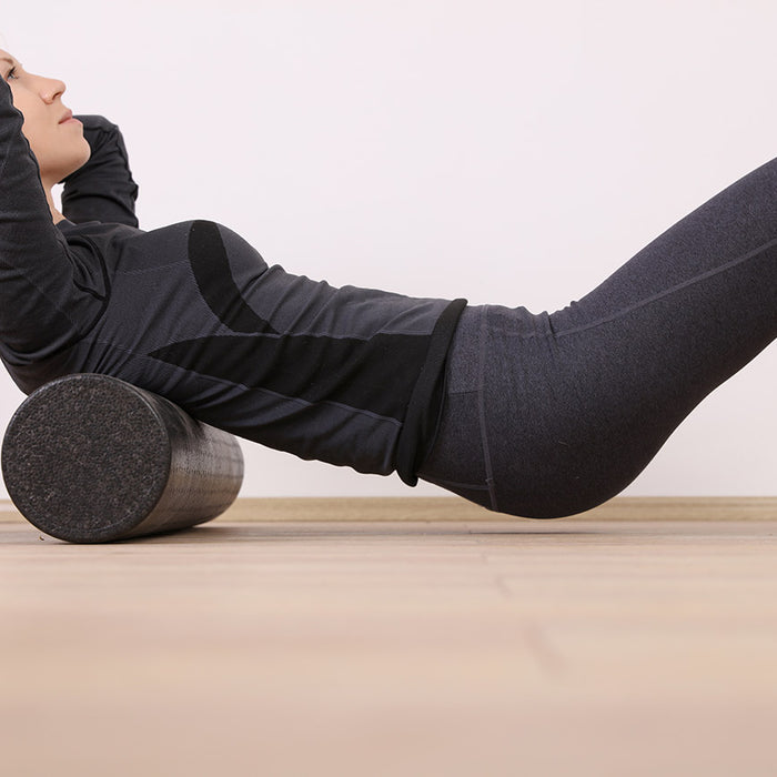 Woman with long blond hair wearing black workout clothes while rolling on a black foam roller