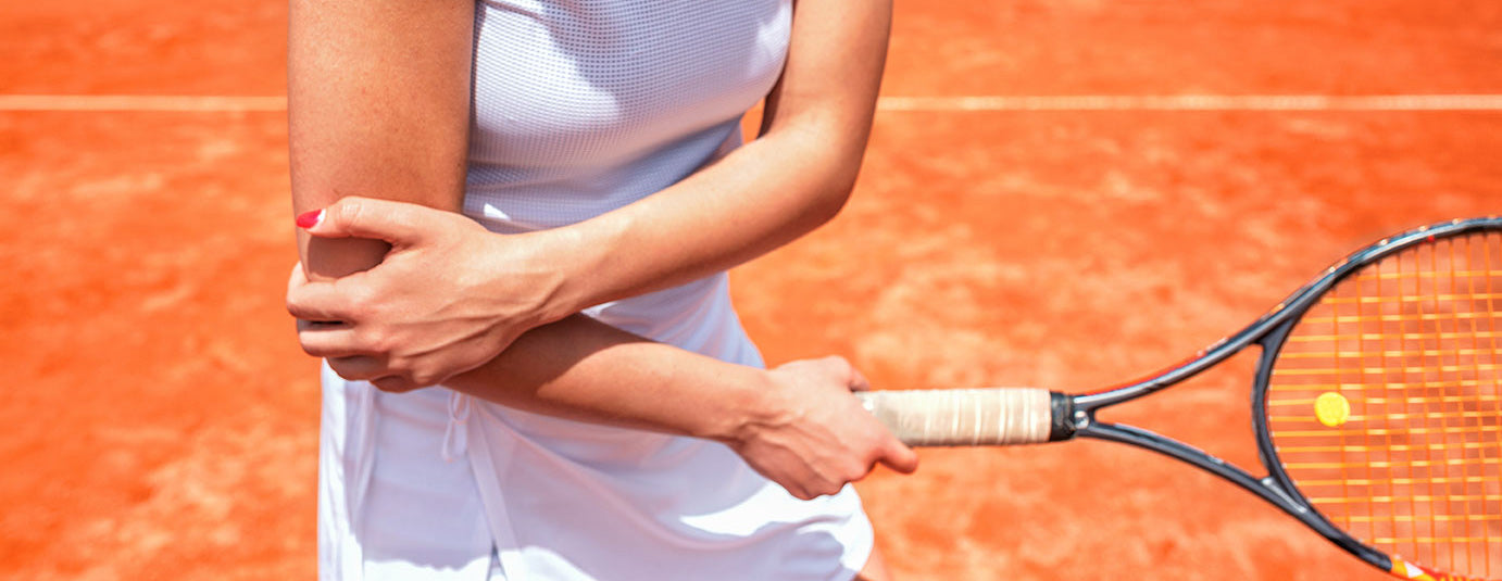 Woman on tennis court looking down at and holding elbow of arm holding tennis racquet