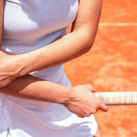 Woman on tennis court looking down at and holding elbow of arm holding tennis racquet