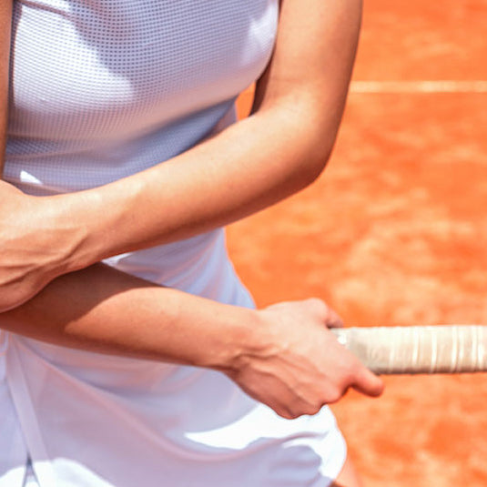 Woman on tennis court looking down at and holding elbow of arm holding tennis racquet