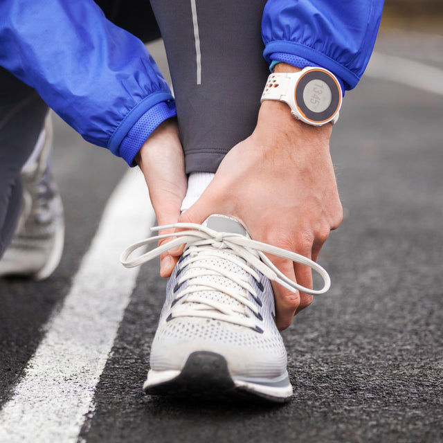 woman holds her ankle from pain after completing her run