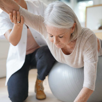 woman physical therapist assists her elderly patient with balance improving exercises