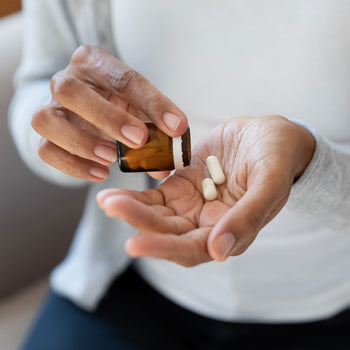 black woman pours 2 nutritional supplement pills into her open palm