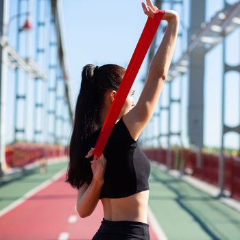 woman athlete uses resistance bands on a track course to improve muscle strength
