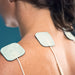 woman applying the electrodes of the Vive Health 5-Mode TENS Unit to her shoulders and back