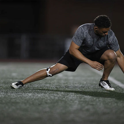 man soccer player stretching on the field while wearing the ProBand KneedIT